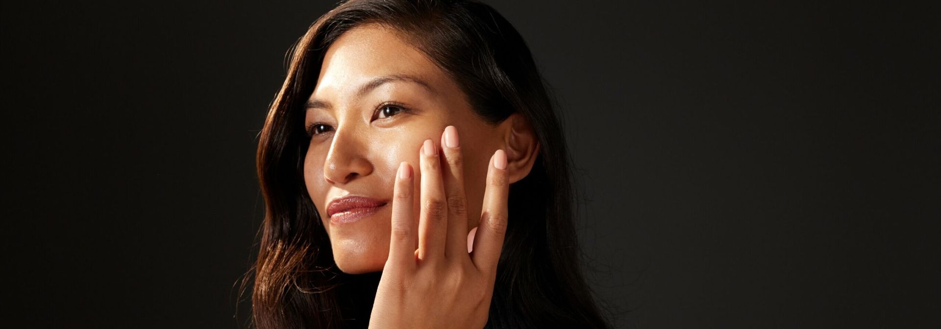 An adult woman touching her cheek with dramatic lighting.